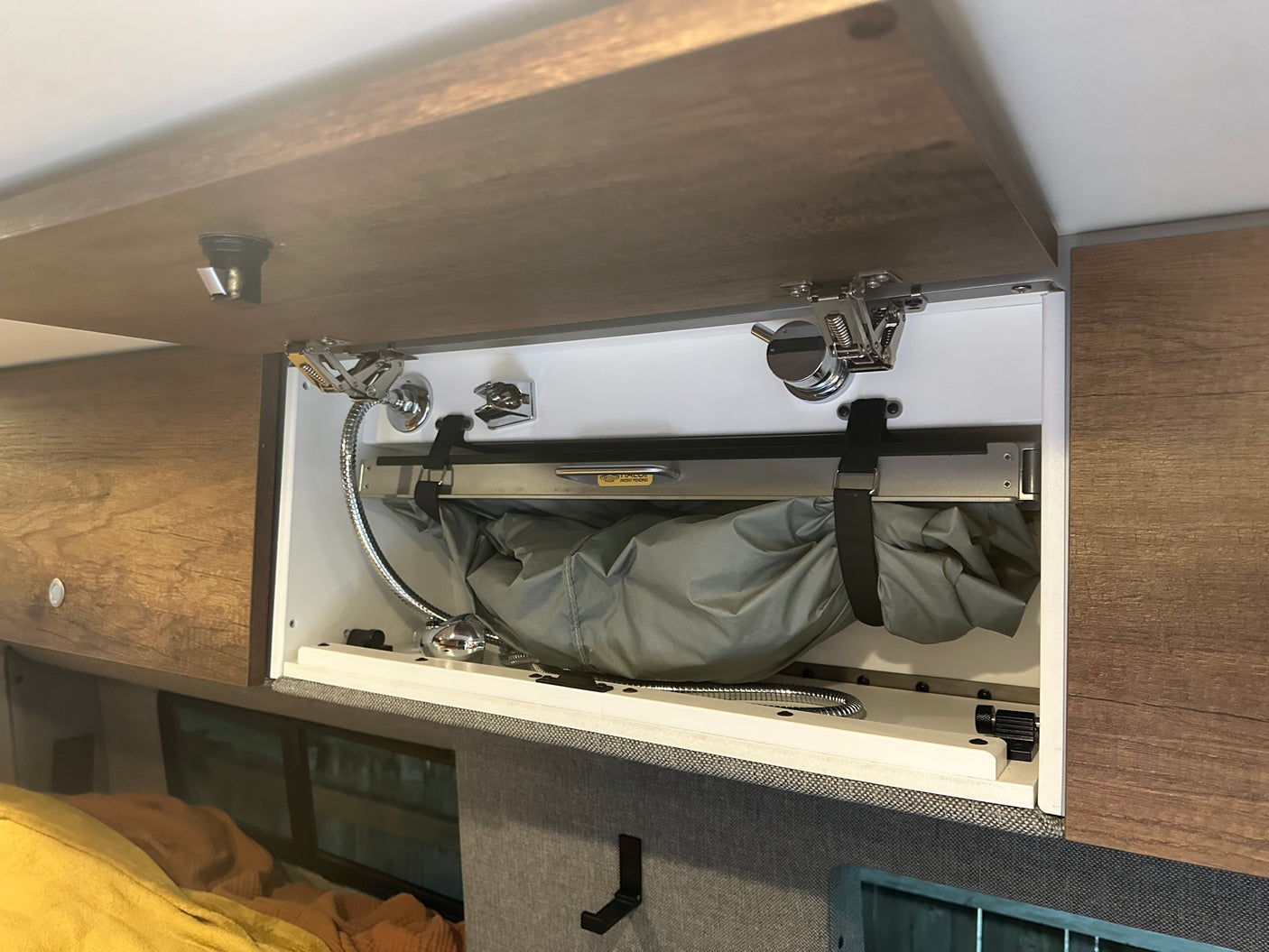 Open overhead cabinet in an rv rental, revealing a neatly stowed portable shower system with hose and showerhead for convenience.