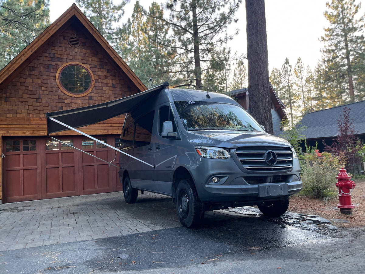 ideal for rv rental road trips and outdoor adventures.|Gray Mercedes Sprinter RV rental with extended awning parked in a paved driveway in front of a rustic wooden house.|A vehicle dashboard screen displays a fuel consumption graph showing an average of 19.0 mpg over 7.5 min. Vital data for any rv rental journey.|Spacious RV rental camper van interior. Features a kitchen with fridge — photo 3