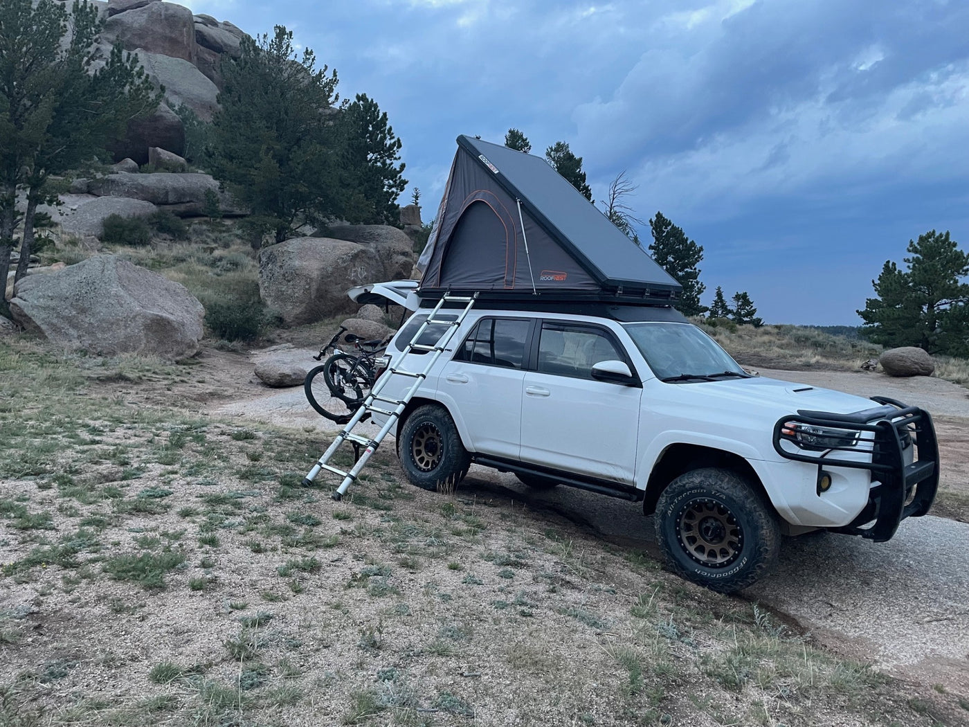 White RV rental SUV with a deployed rooftop tent, ladder, and bike, parked in rocky wilderness ready for adventure. — photo 13