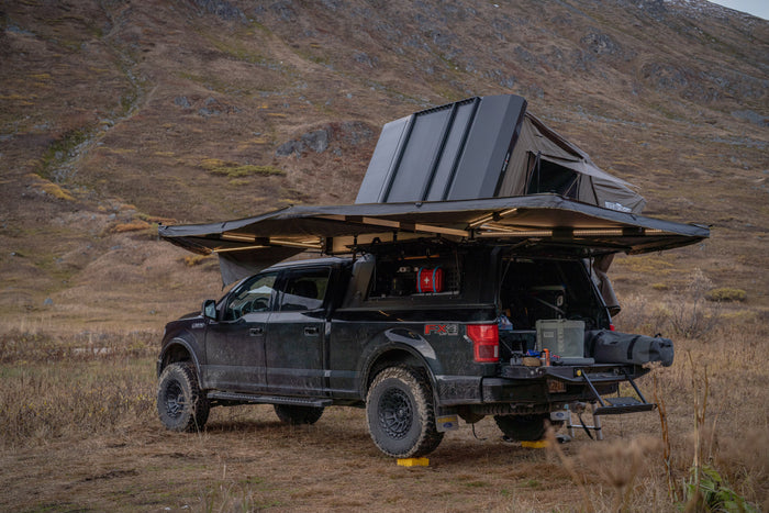 This rugged overlanding Ford F-150, equipped with a rooftop tent and lighted awning, offers the ultimate RV rental adventure in nature.