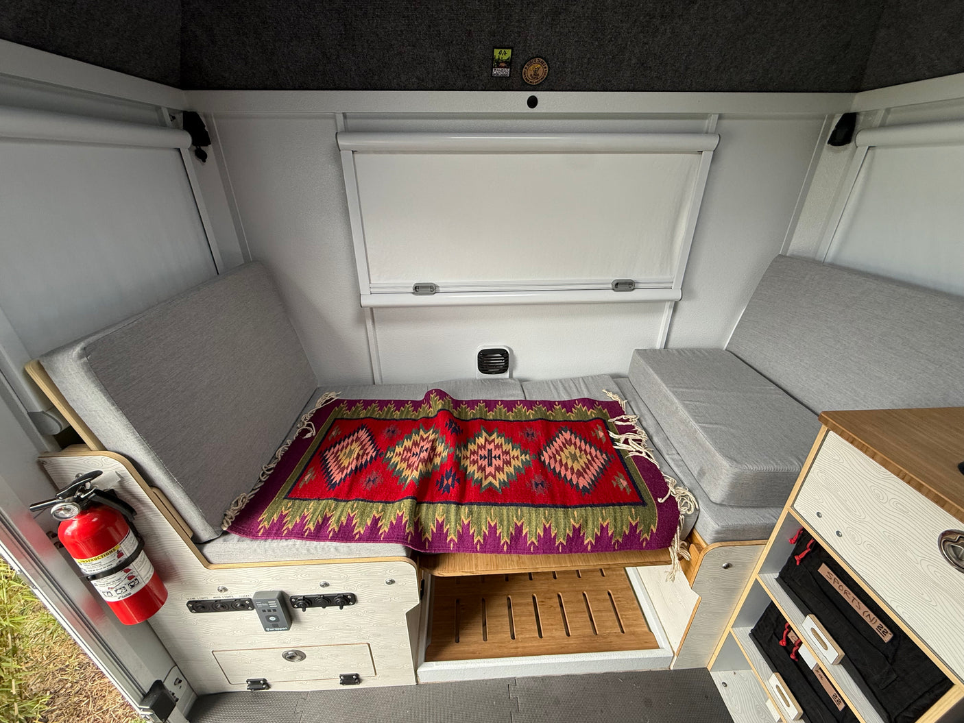 Inside an rv rental: grey benches, colorful rug, fire extinguisher, and controls. Compact and functional space.