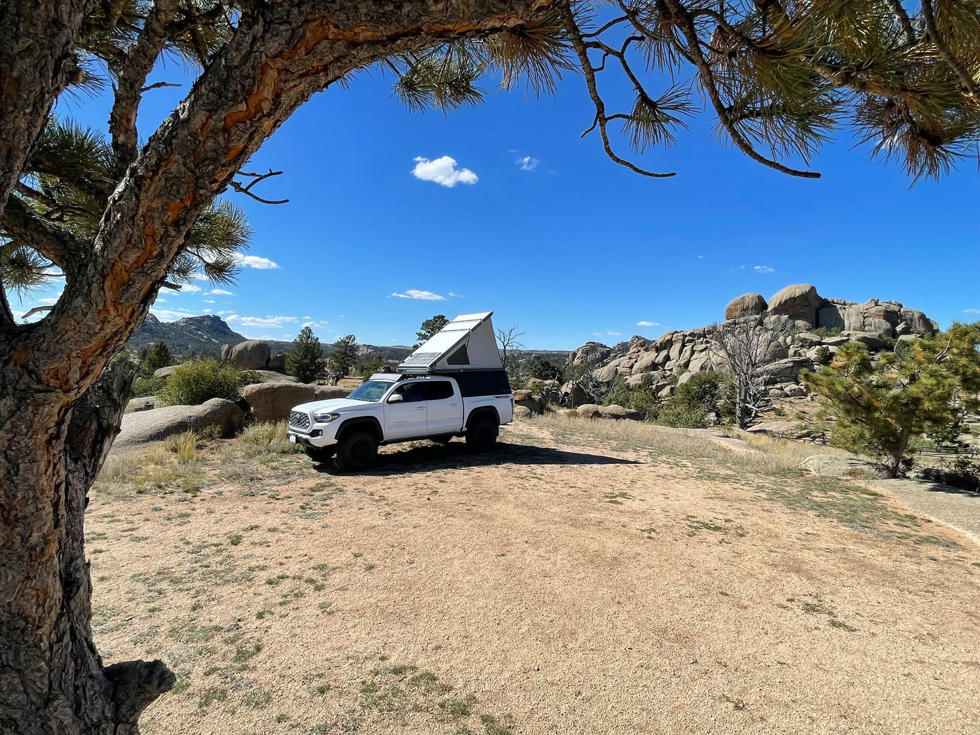 Overland white truck with pop-up camper at a scenic rocky campsite. Perfect for your rv rental escape!