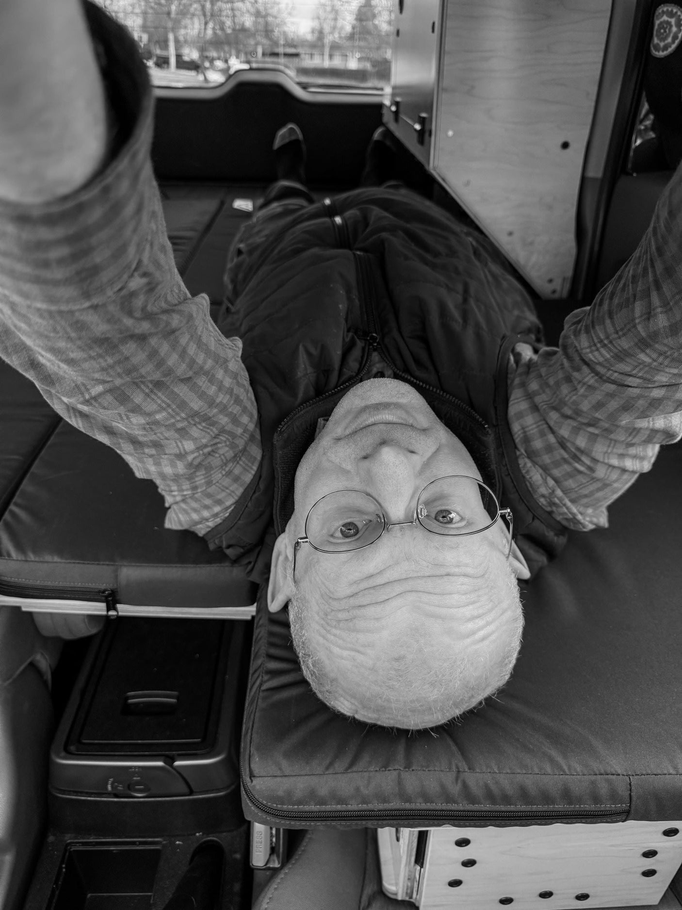 Man with glasses relaxing on the comfy bed of an RV rental campervan conversion, arms overhead.