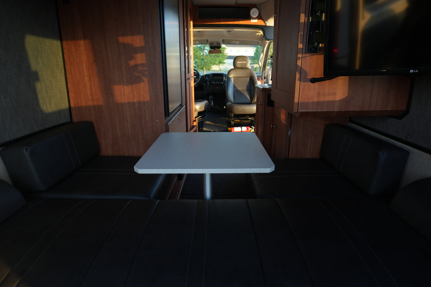 Interior of an RV rental showing a bright dinette with dark cushioned benches, wooden cabinetry, and the front cabin view.