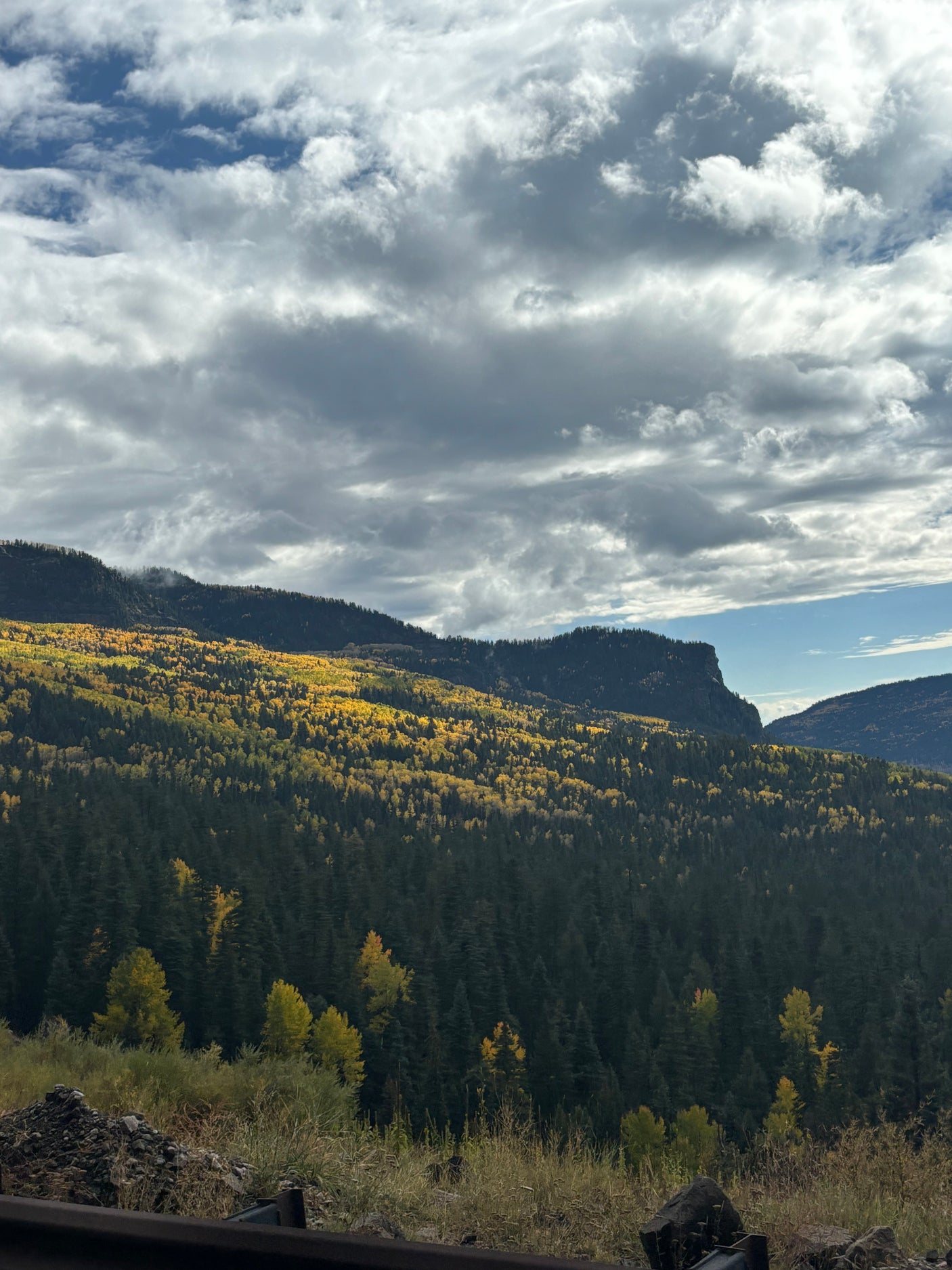 Experience fall mountain beauty! Vibrant yellow aspens and dark green evergreens blanket mountains under a dramatic sky. Ideal RV rental scenery.