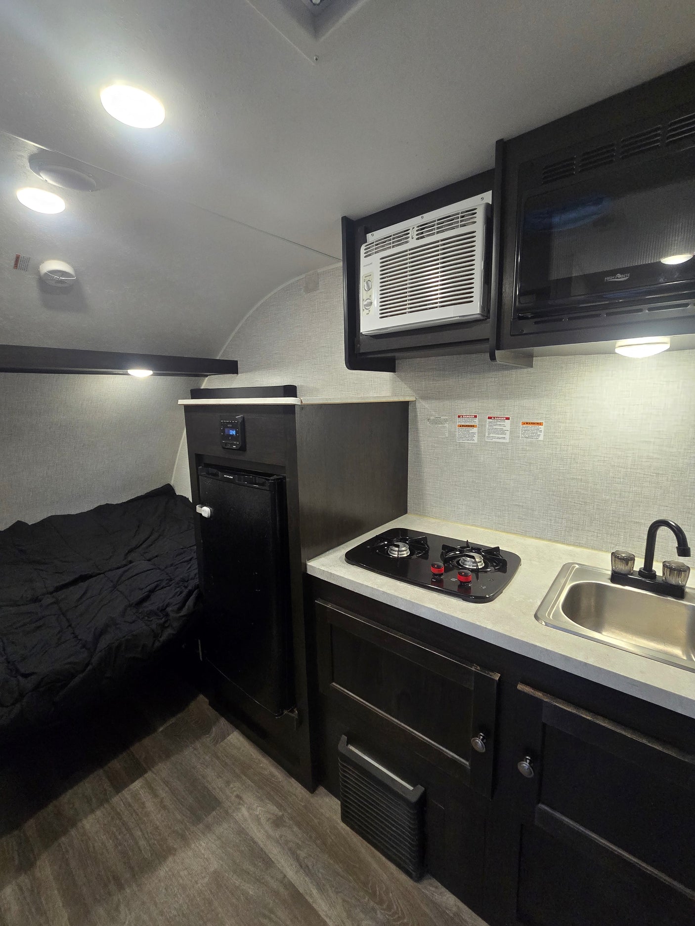 Inside an RV rental: features a bed, compact kitchen with sink/stove, fridge, microwave, and AC unit.
