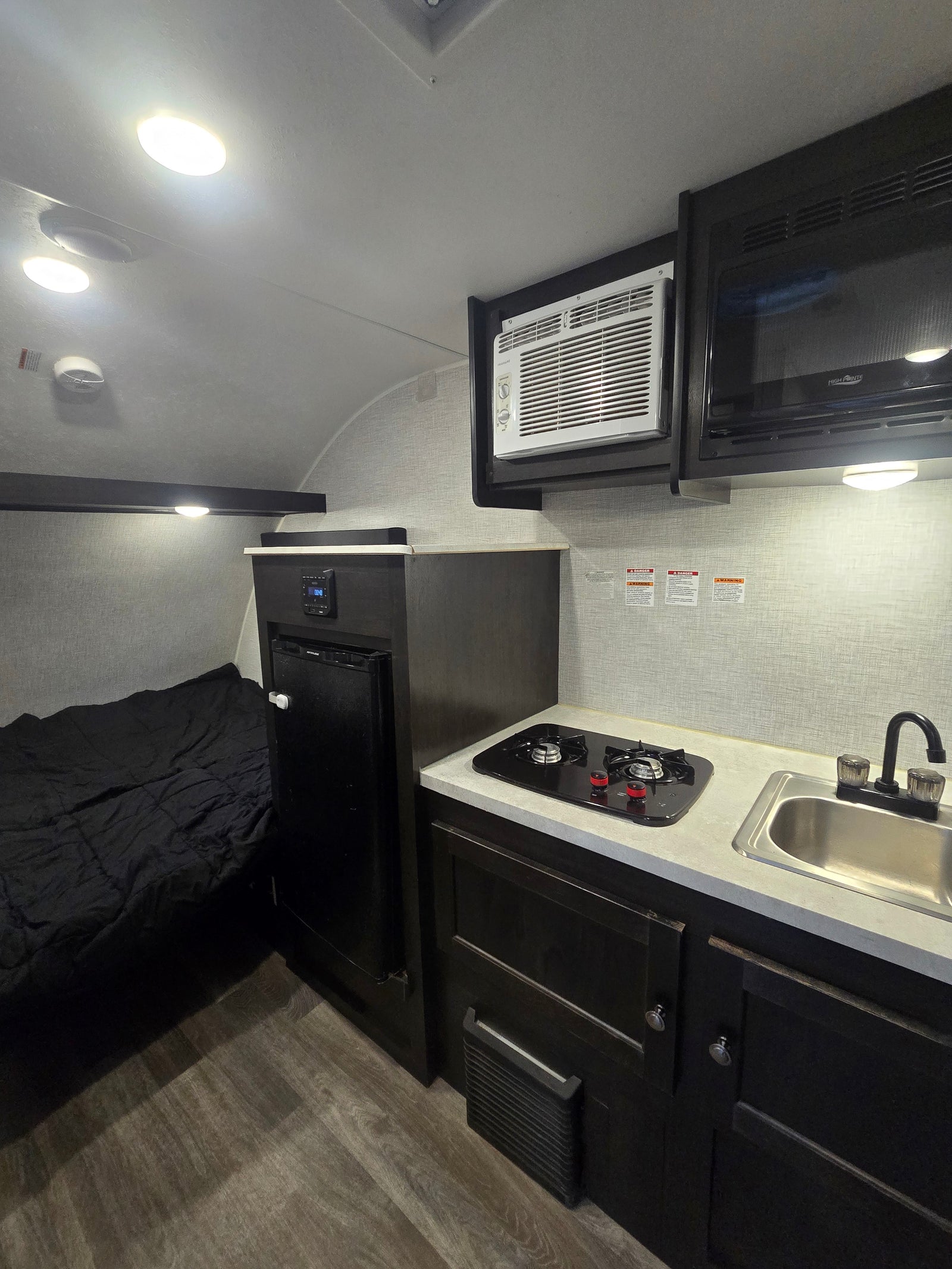 Inside an RV rental: features a bed, compact kitchen with sink/stove, fridge, microwave, and AC unit.