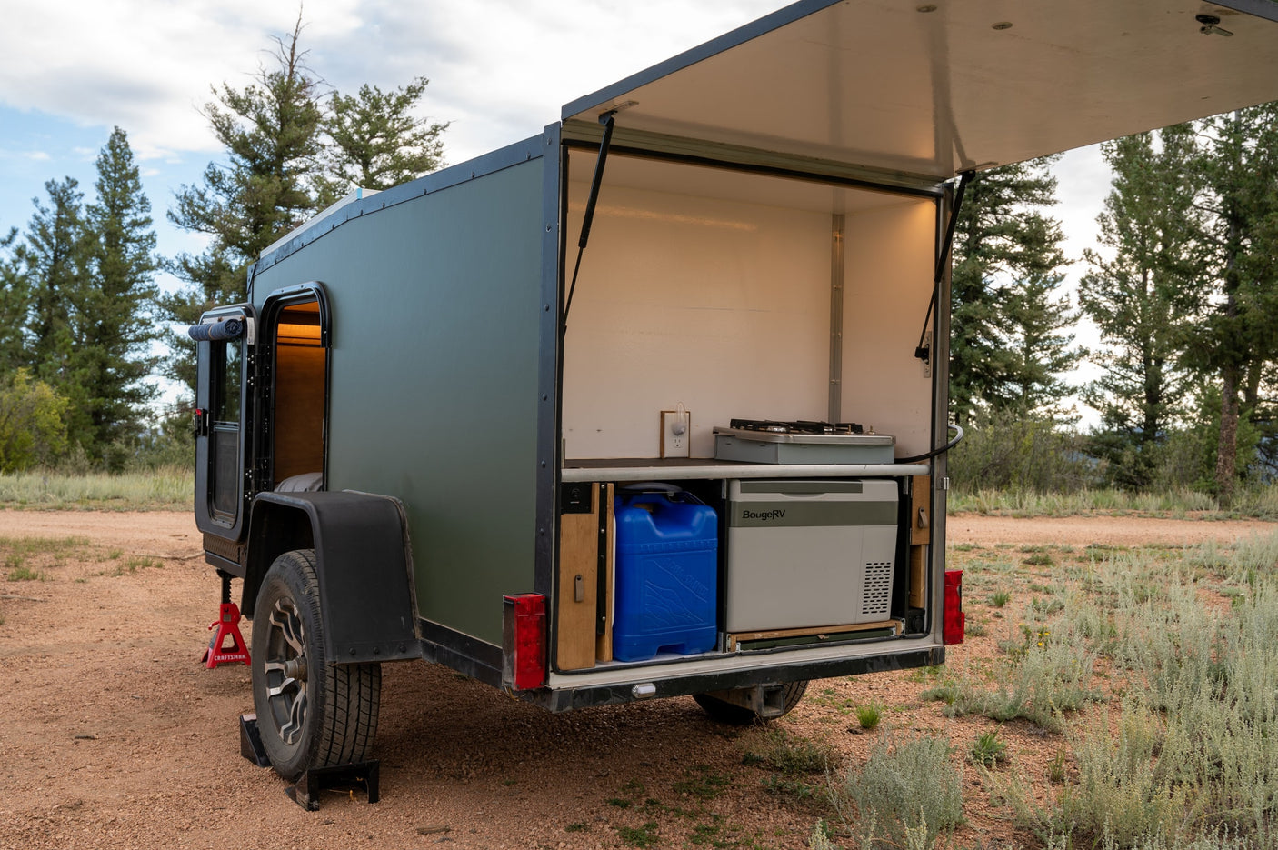 This compact green rv rental trailer features an open rear galley with a portable fridge & stove, ideal for outdoor camping.