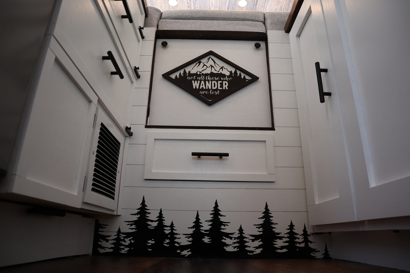 Modern RV rental interior with custom white cabinets, shiplap walls, a "Wander" sign, and pine tree accents.