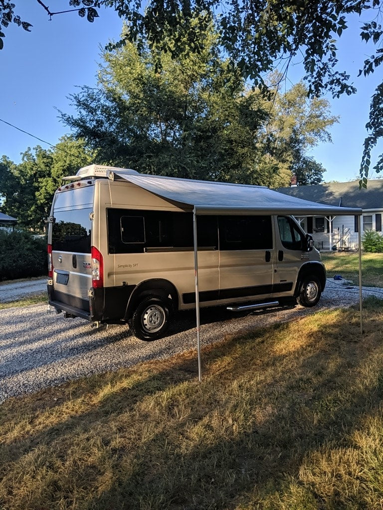 Light tan RV rental with extended awning on gravel driveway