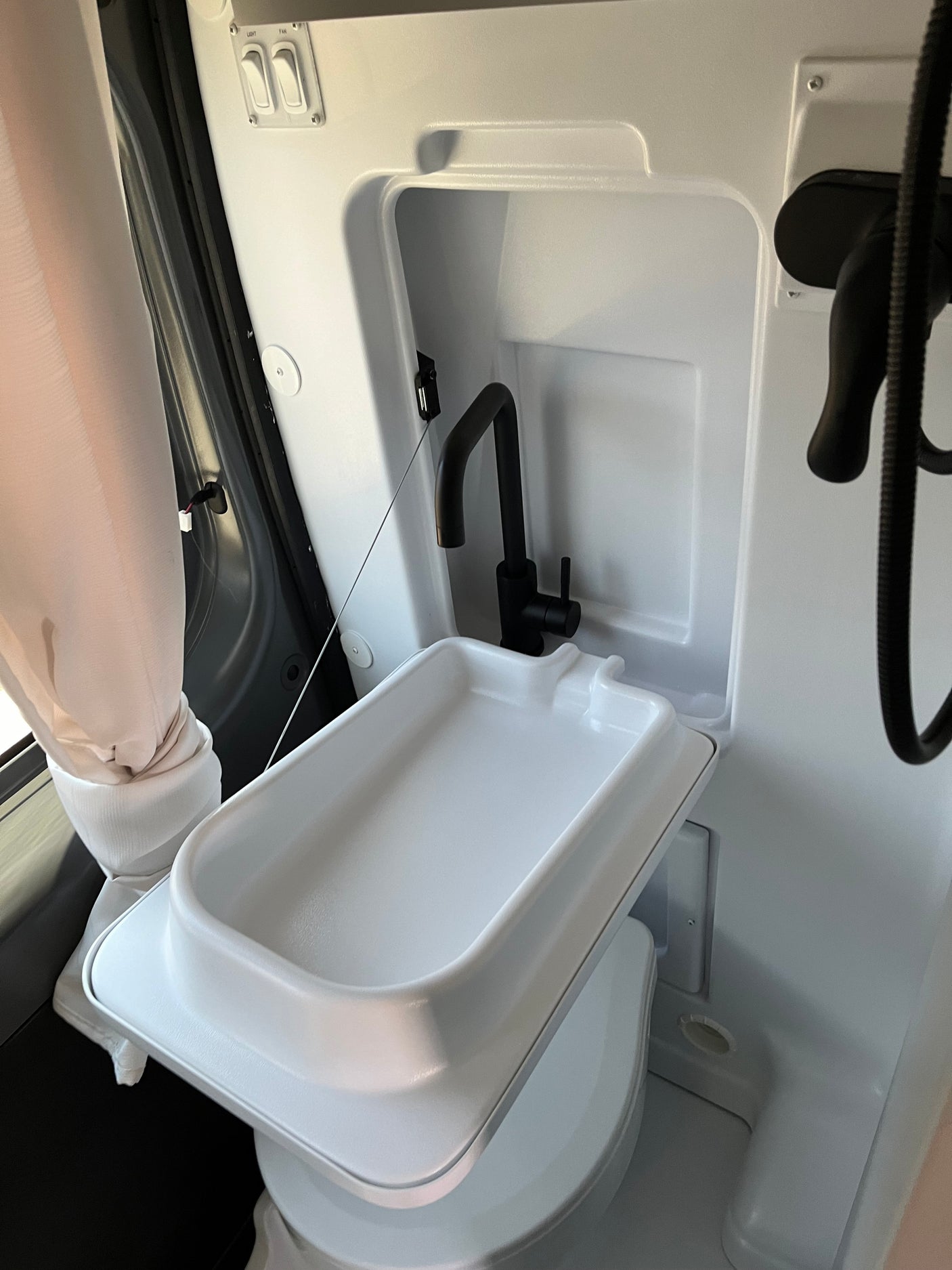 Compact RV rental bathroom with foldable sink, black faucet, and shower setup for efficient space use.