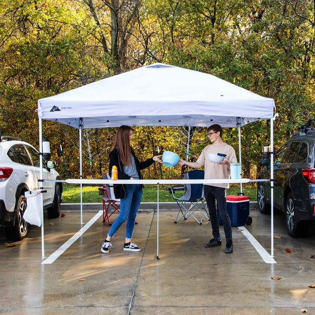 Two people share food under a white canopy tent, tailgating in a parking lot. An ideal setup for an RV rental outdoor event.