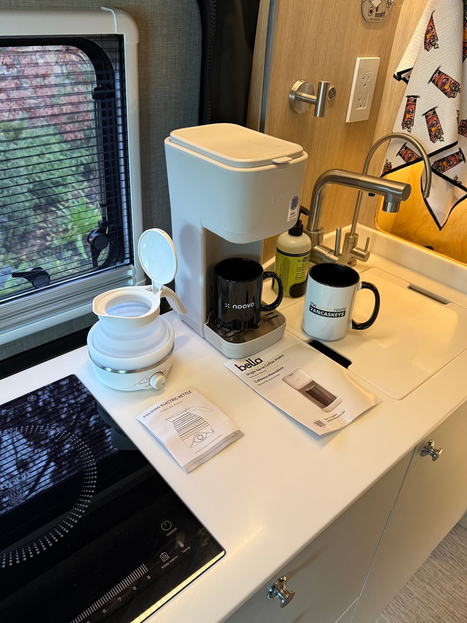 An rv rental's compact kitchen with a Bella coffee maker, folding electric kettle, induction cooktop, and sink area.