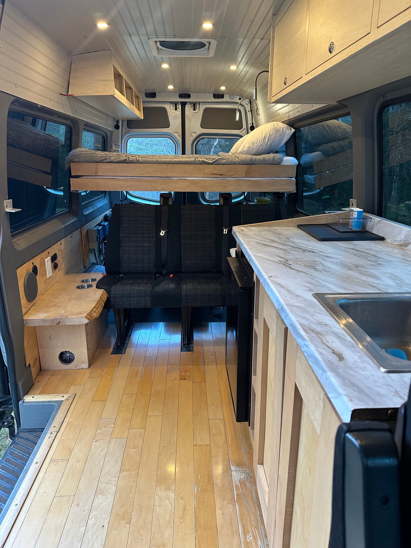 RV rental: custom wood interior featuring elevated bed, kitchen, and rear seating area.