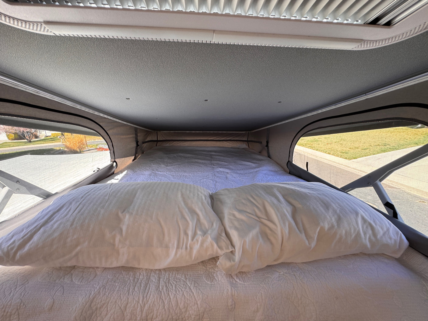 Cozy pop-top bed in an RV rental, featuring soft pillows, a blanket, and open side windows for a comfortable view.