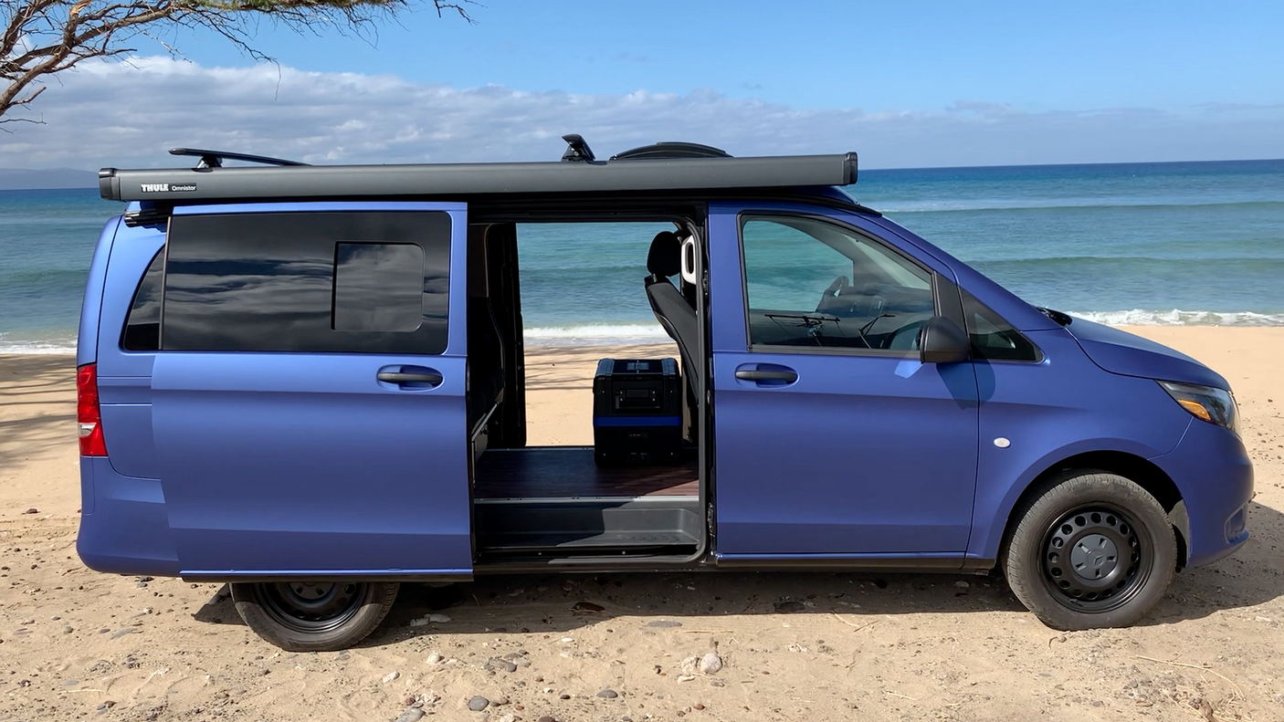 Blue campervan on sandy beach, side doors open to ocean view. Perfect rv rental for coastal adventures.
