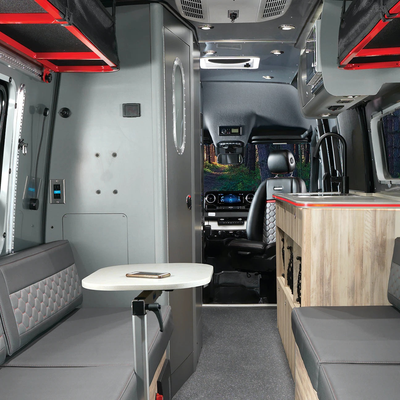 Modern camper van interior for RV rental, featuring a kitchen, seating with table, and driver's cabin view.
