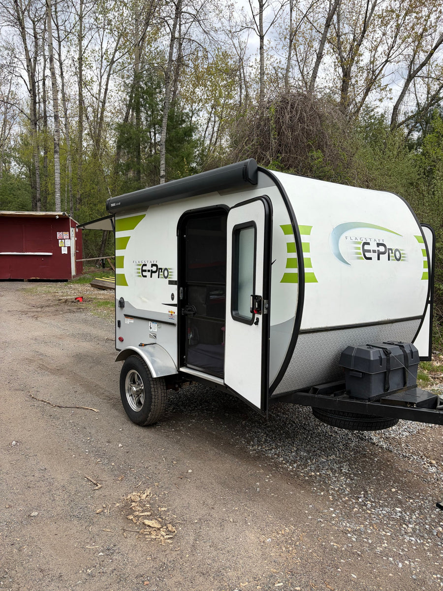 RV rental: A white and green Flagstaff E-Pro travel trailer with its door open, parked on a gravel lot.