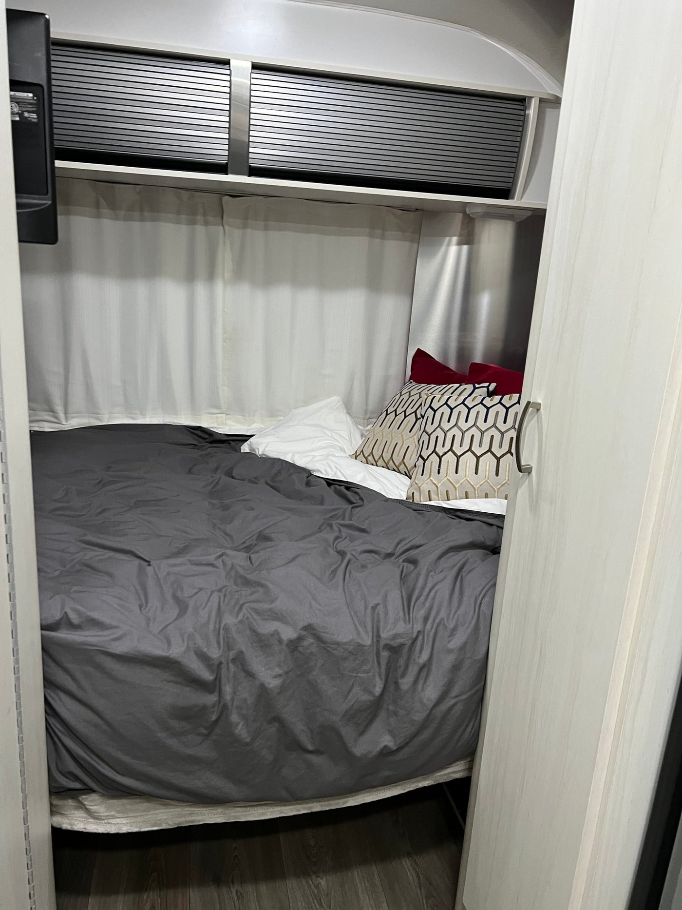 Inside an RV rental: a compact bedroom featuring a bed with grey duvet, patterned pillows, and sleek overhead cabinets. — photo 11