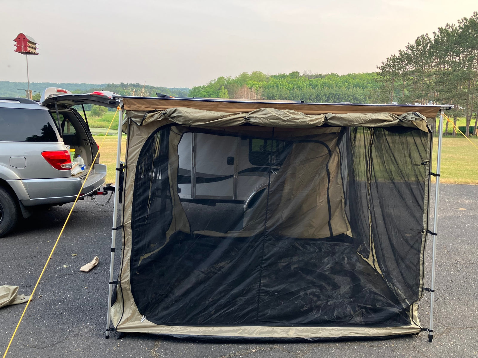 RV rental camp: SUV with awning & screen room enclosing a camper, providing shaded outdoor space.