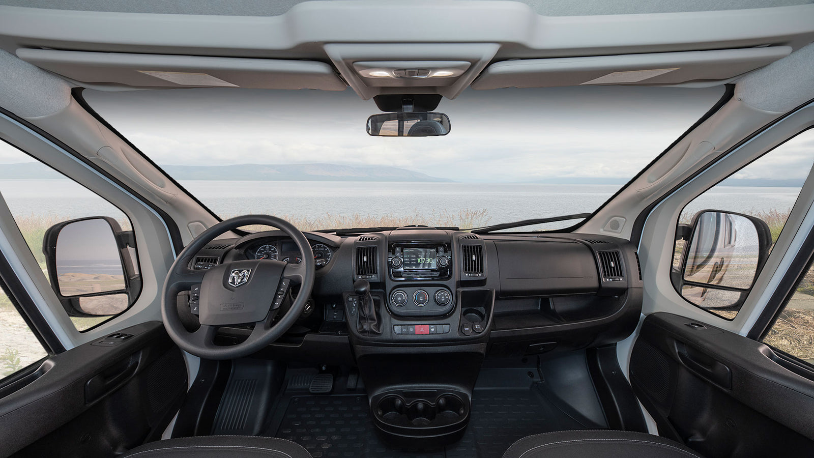 RV rental: Inside a camper van's cockpit, showing the dashboard, steering wheel, and a scenic waterfront view ahead.