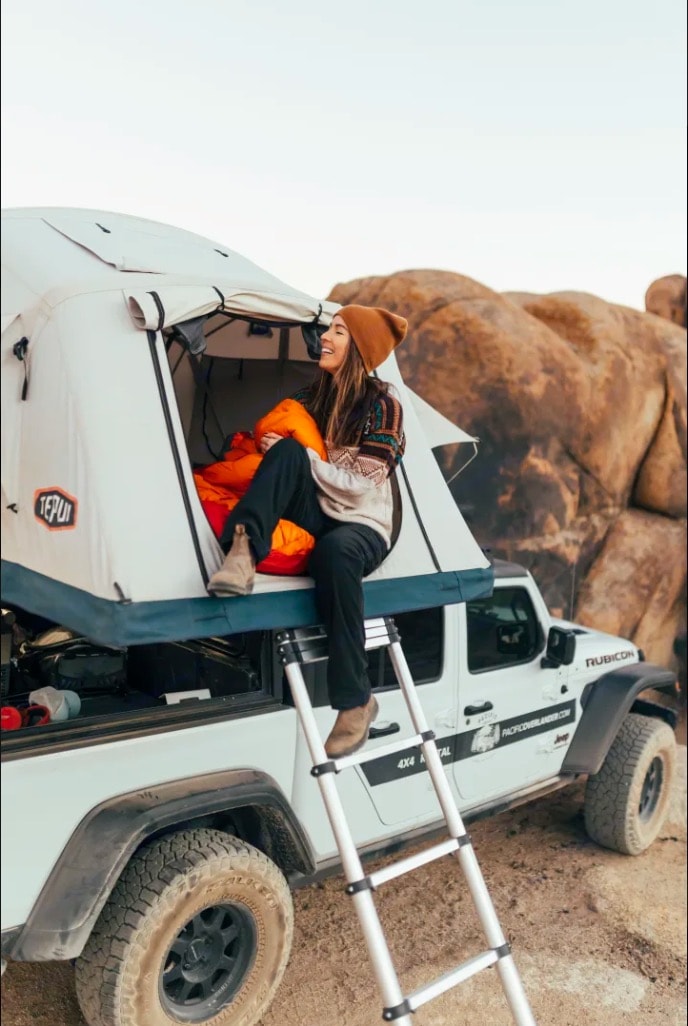 showcasing a unique RV rental for desert adventures.|Enjoy an RV rental trip! A man cooks next to his Jeep & Tepui rooftop tent