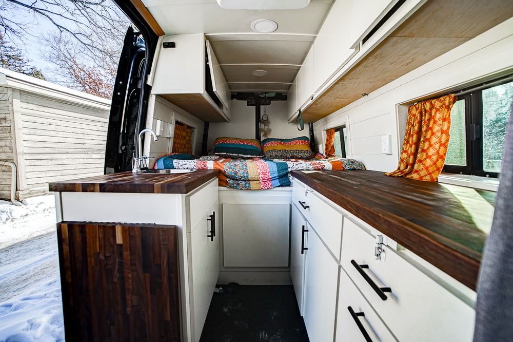 and side storage box with Thule mounts for adventure gear.|A black rv rental camper van is parked on a mountain road beside a lake