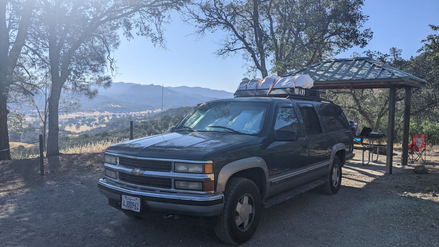 Dark green SUV, packed with gear, at a scenic campsite overlooking a valley. Great for an outdoor trip like an RV rental.