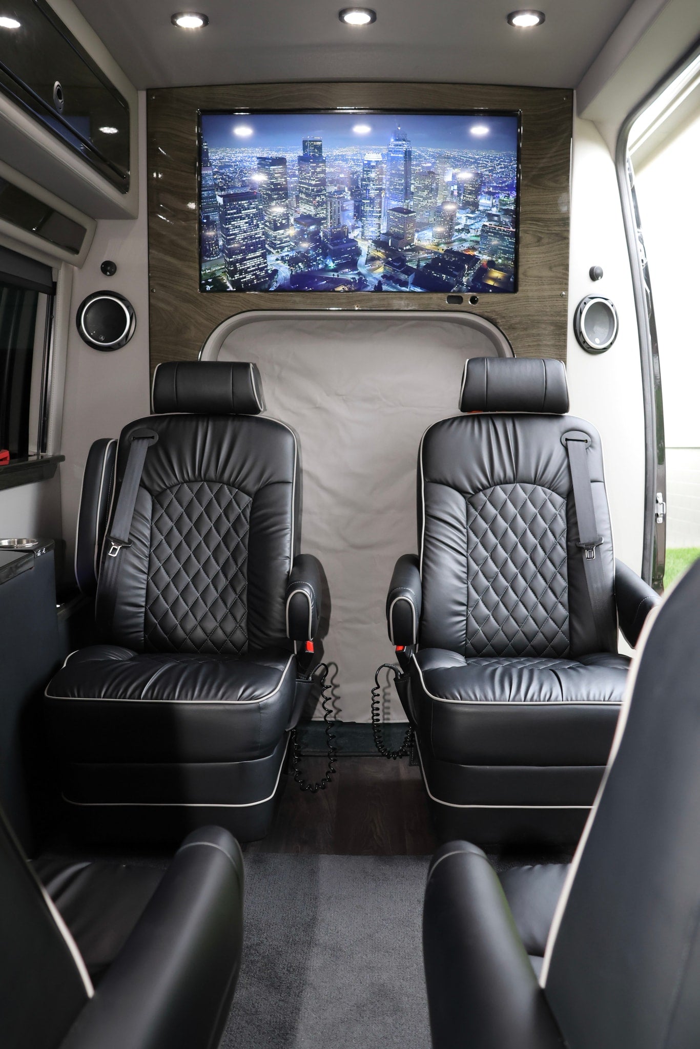Plush black captain's chairs and a large screen displaying a city skyline define this luxurious rv rental interior.