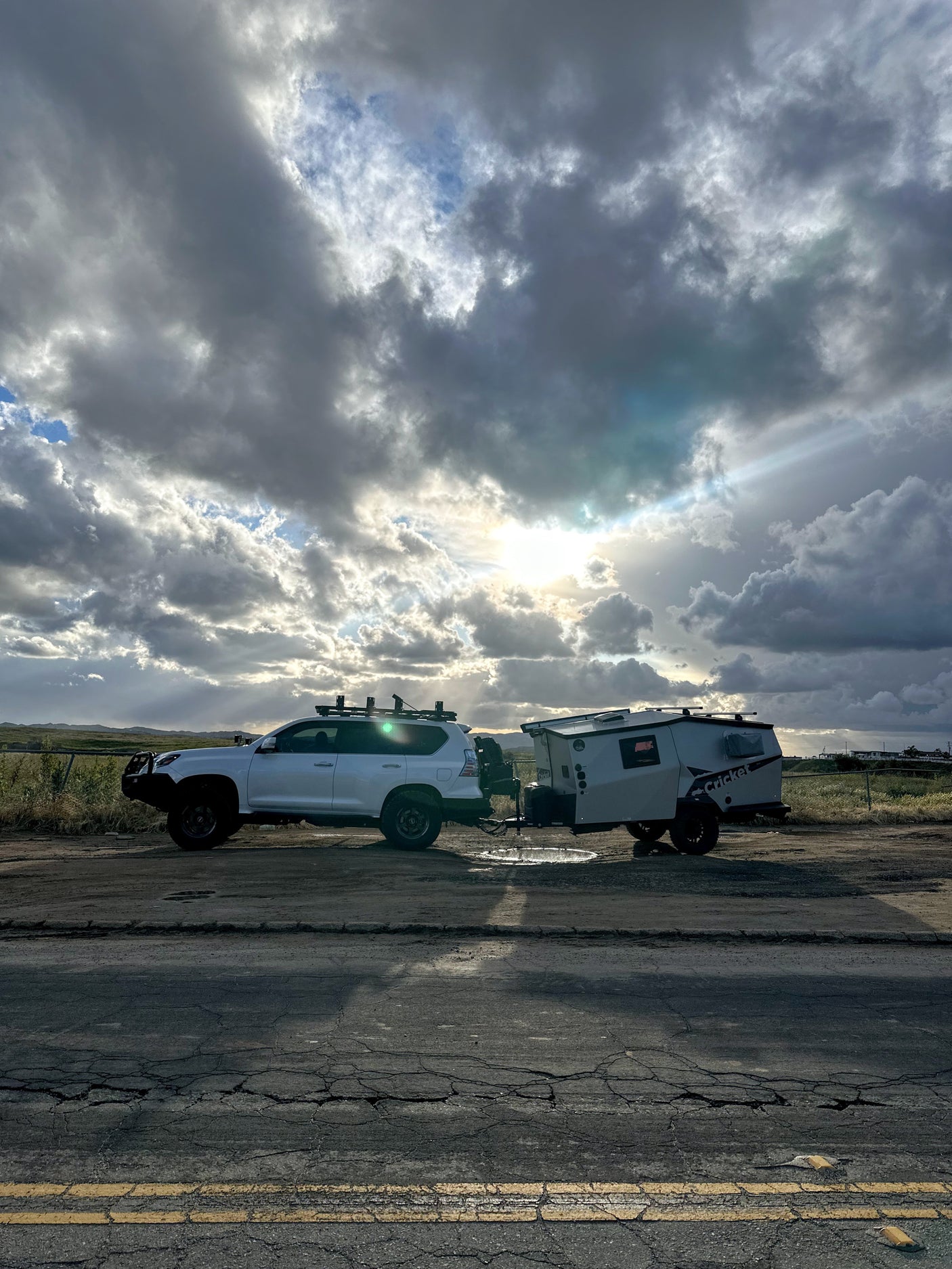 Overland SUV towing a Cricket camper, ideal for your next rv rental adventure. Dramatic clouds with sun rays on a dirt road.