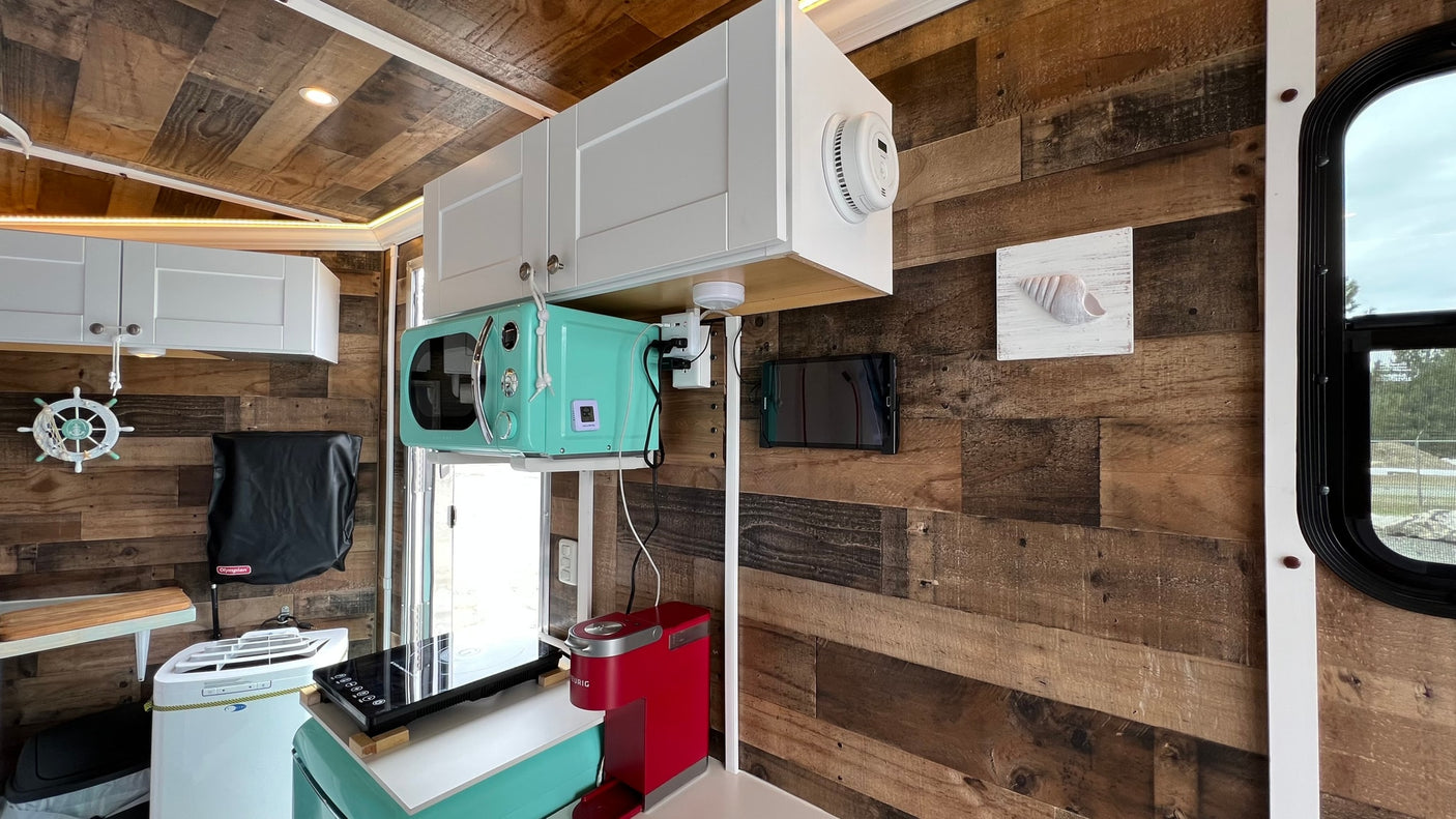 RV rental kitchen: wood walls, white cabinets, retro mint microwave, coffee maker, cooktop, and nautical decor.