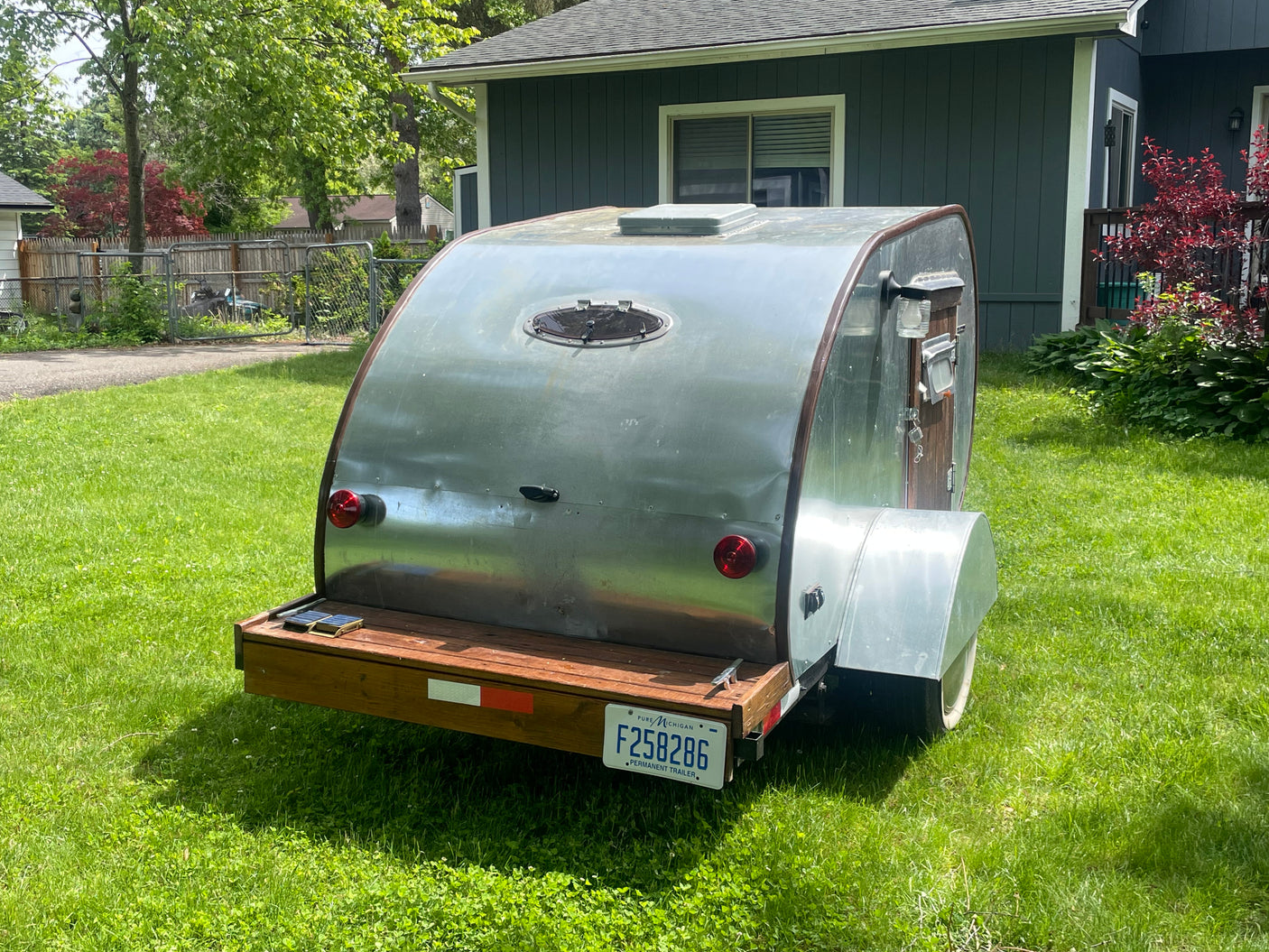 Shiny aluminum teardrop camper on a lawn, perfect for an RV rental. Michigan F258286 license plate.