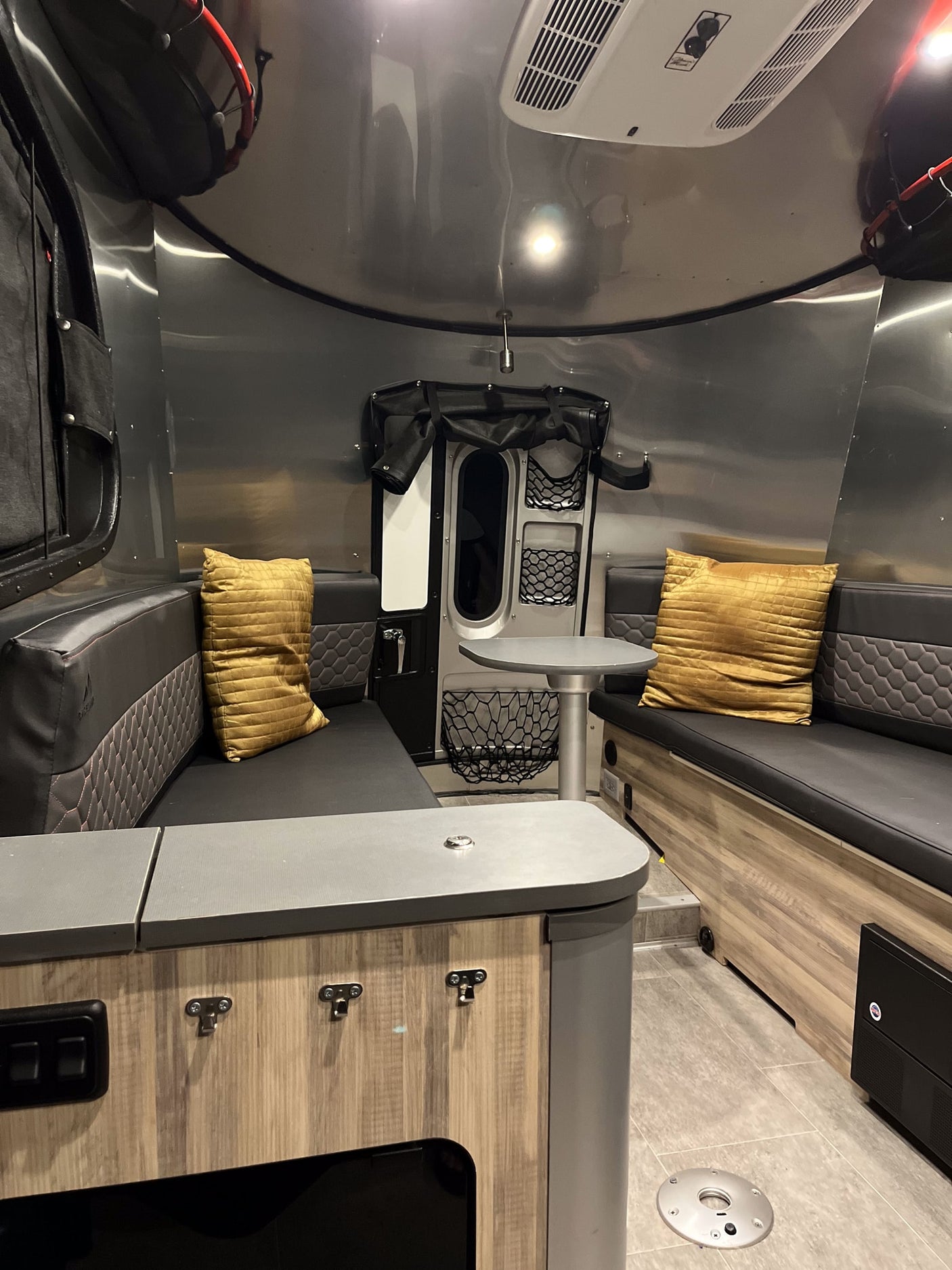 An RV rental's cozy interior, showcasing black and gray upholstered benches, a dinette table, and sleek aluminum walls.