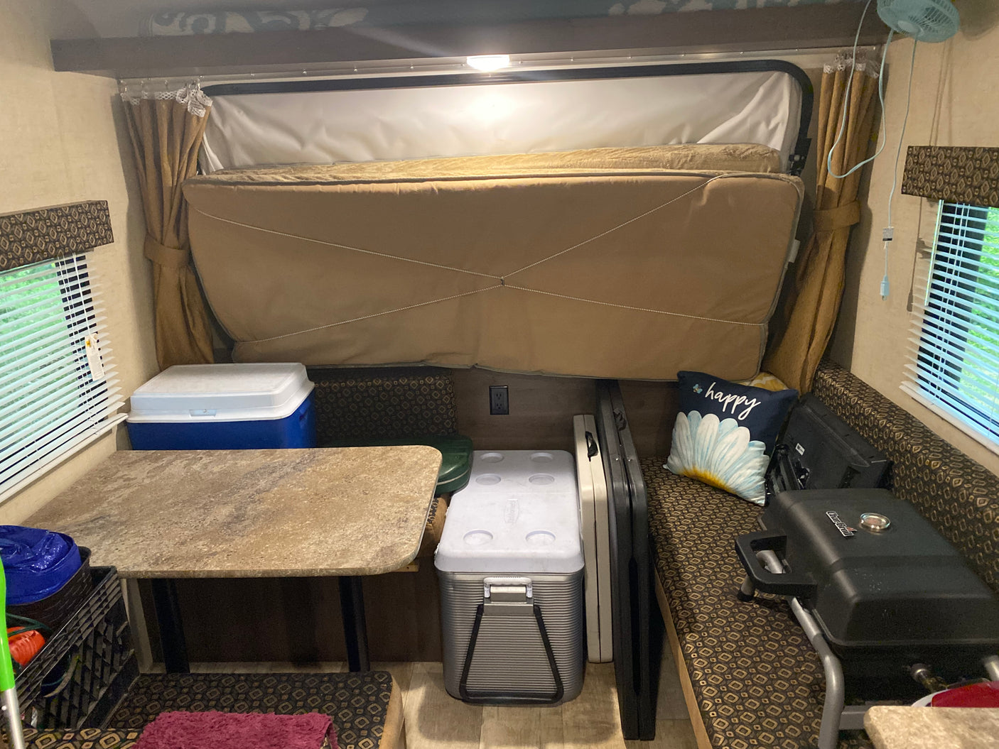 Inside a compact RV rental, featuring a comfortable bed, table, and seating with coolers and a grill.