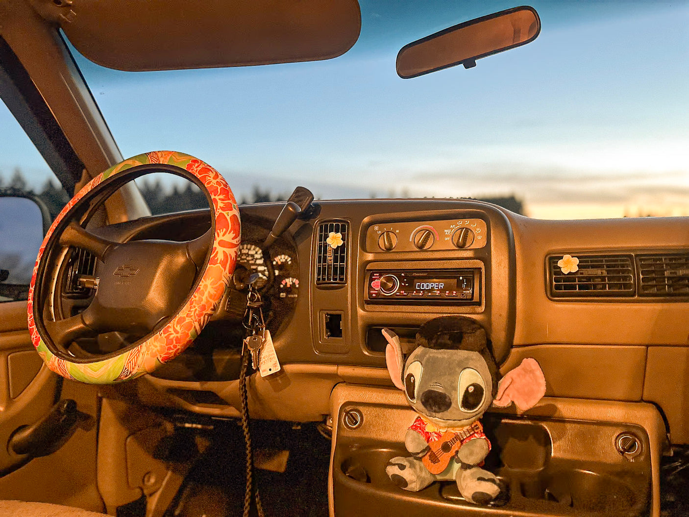 Cozy RV rental interior at dusk: floral steering wheel, Stitch plush, & keys ready for adventure.