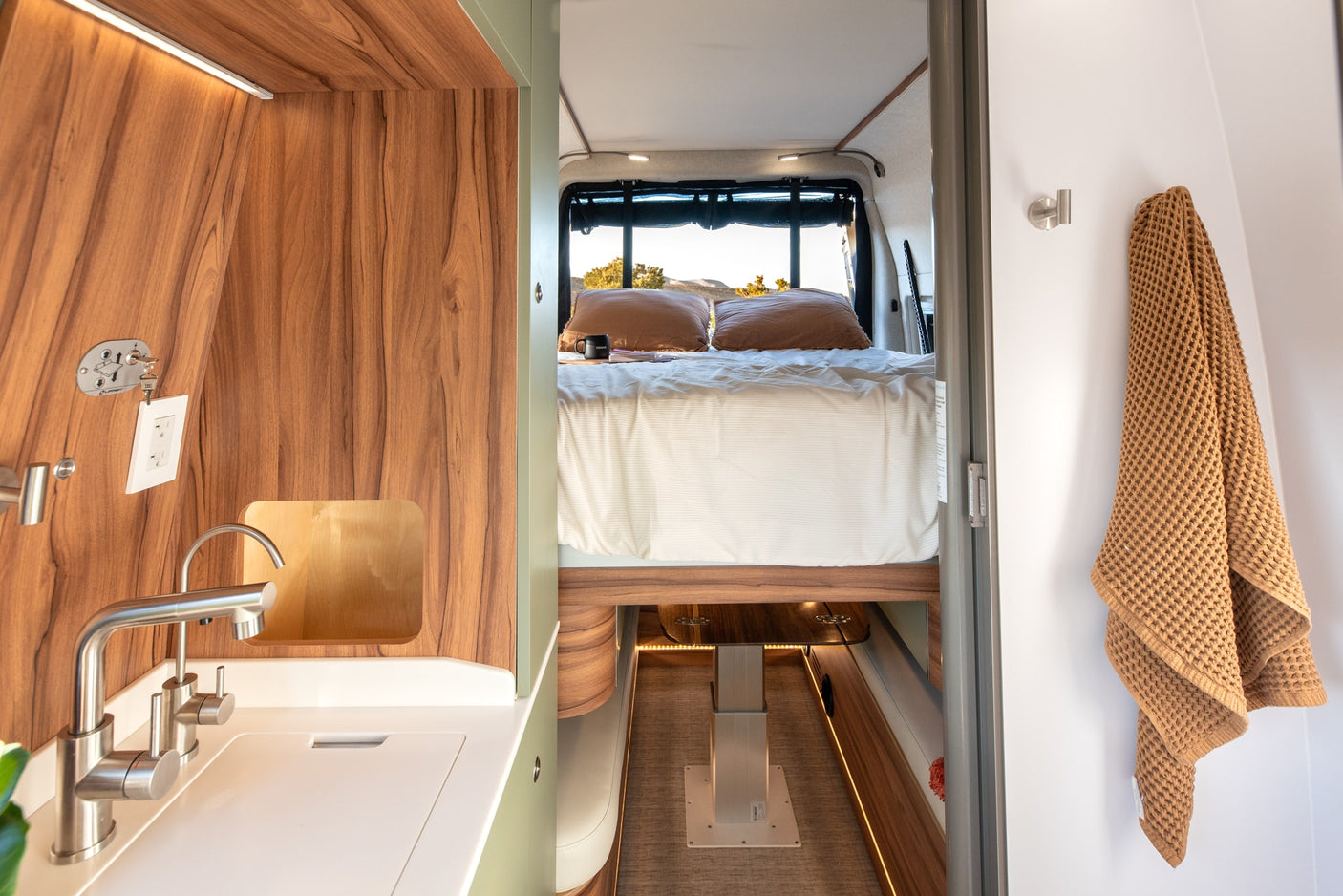 Explore this RV rental's interior: a modern kitchenette, cozy bed, and practical towel hook. Perfect for your next adventure.