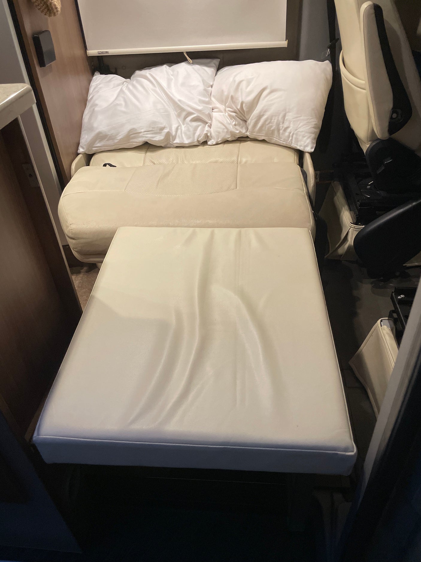 RV rental interior showing a cream convertible bed/seating area with pillows and an ottoman for extended comfort.