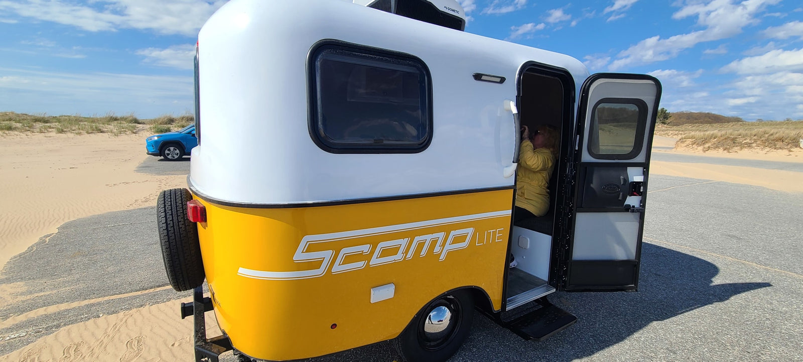 Scamp Lite RV rental parked by sandy dunes. Person inside this compact travel trailer enjoying the view.
