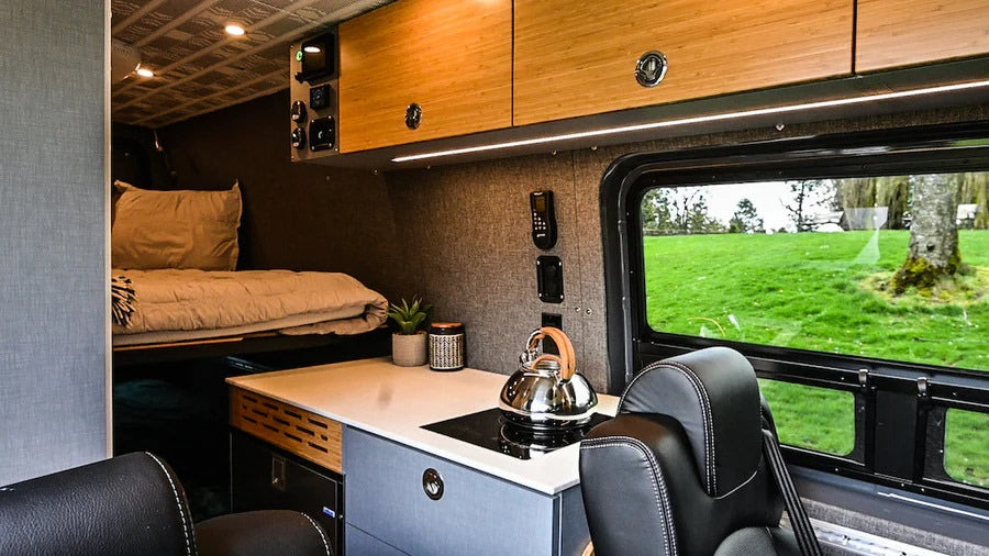 This RV rental interior highlights a bunk bed, compact kitchen with a stove, wooden cabinets, and a scenic window view.