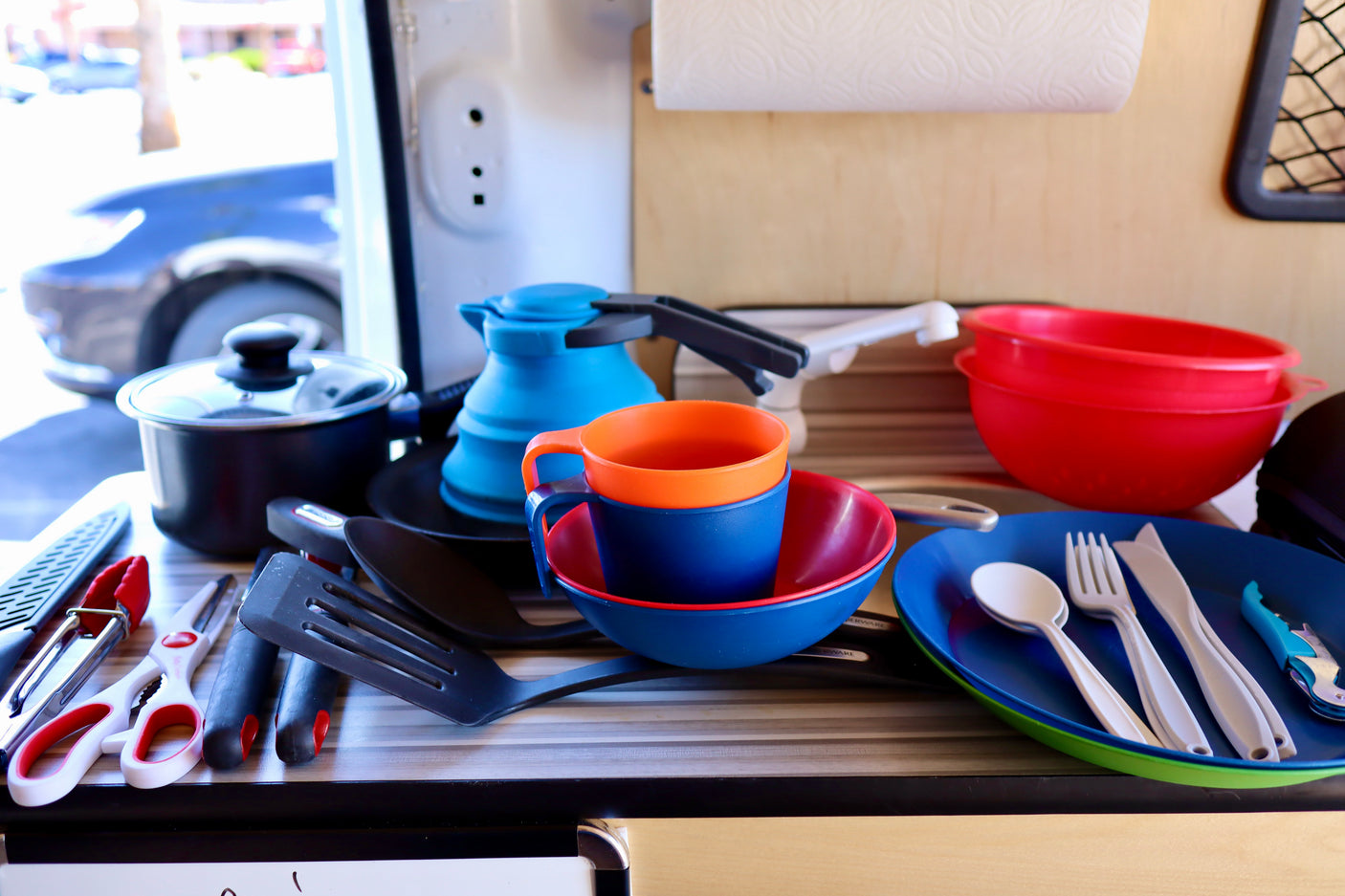 RV rental kitchen setup: a pot, blue collapsible kettle, colorful cups, bowls, and utensils neatly arranged for travel cooking.