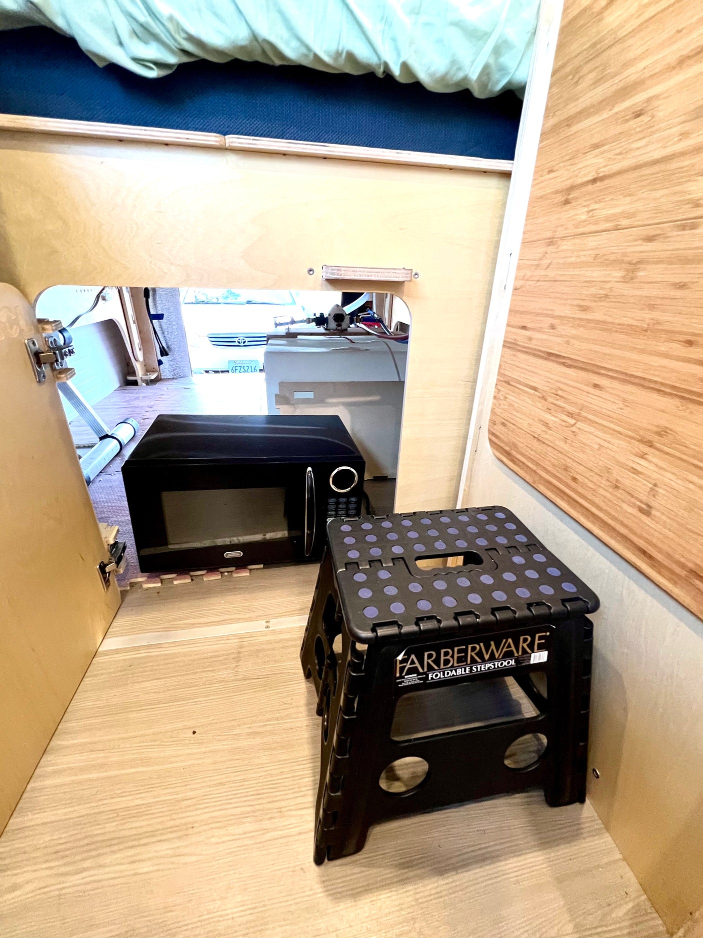 RV rental interior: Microwave & foldable step stool inside a compact camper setup with light wood walls.