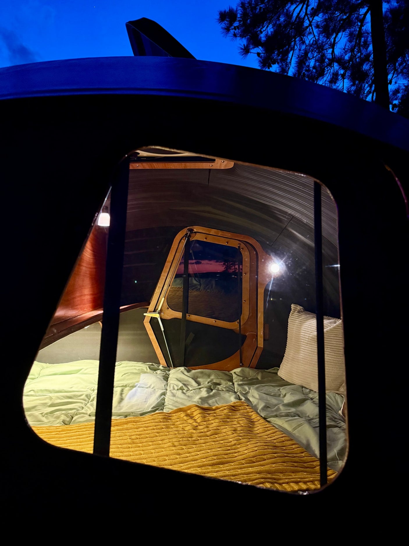 has its doors open at golden hour.|Cozy RV rental view: a bed inside a teardrop camper looking out at a brilliant lake sunset over the water.|Peaceful lakeside RV rental spot with picnic table