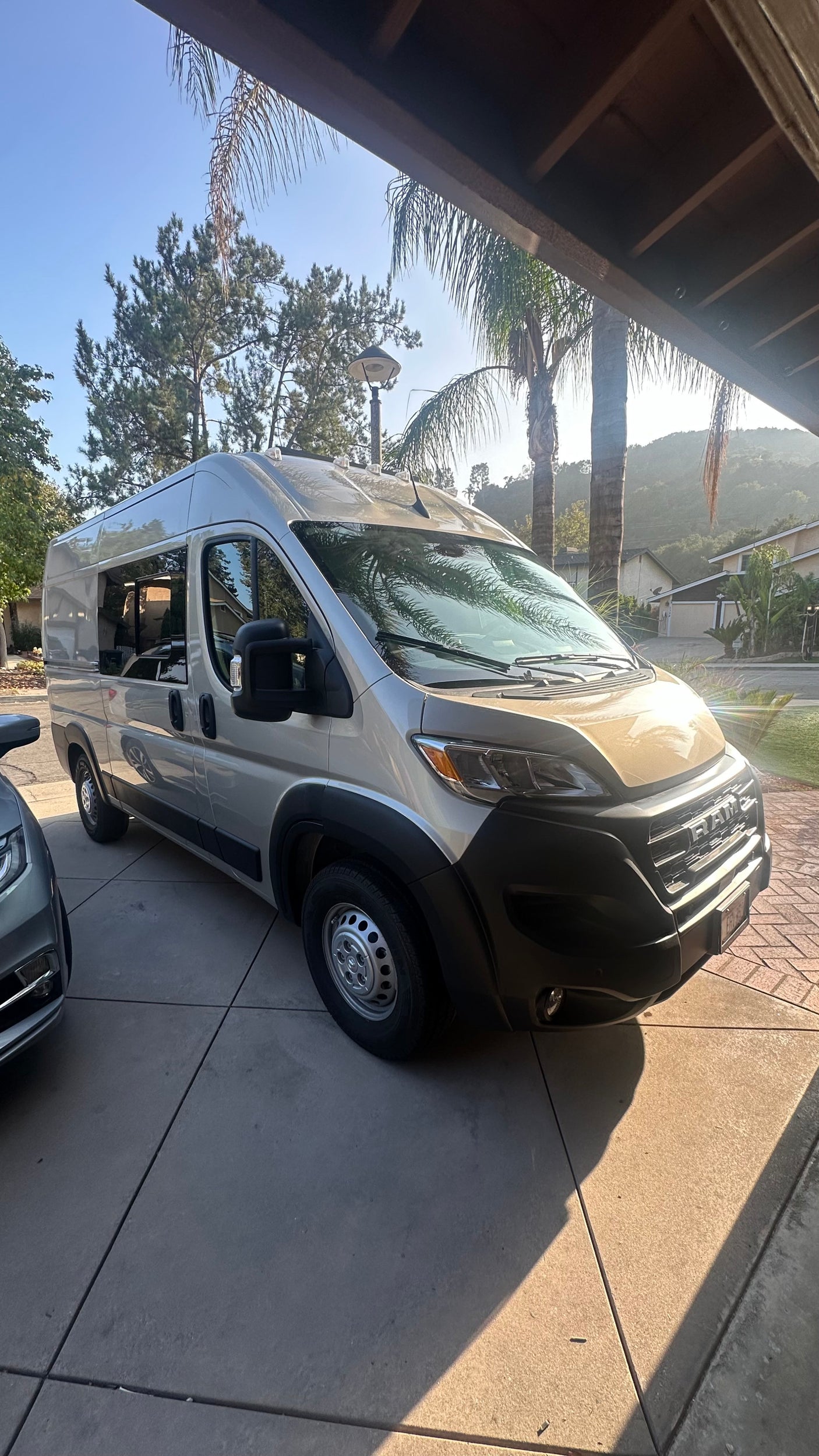 A gold Ram ProMaster camper van, ready for an RV rental, parked on a concrete driveway under a clear sky.