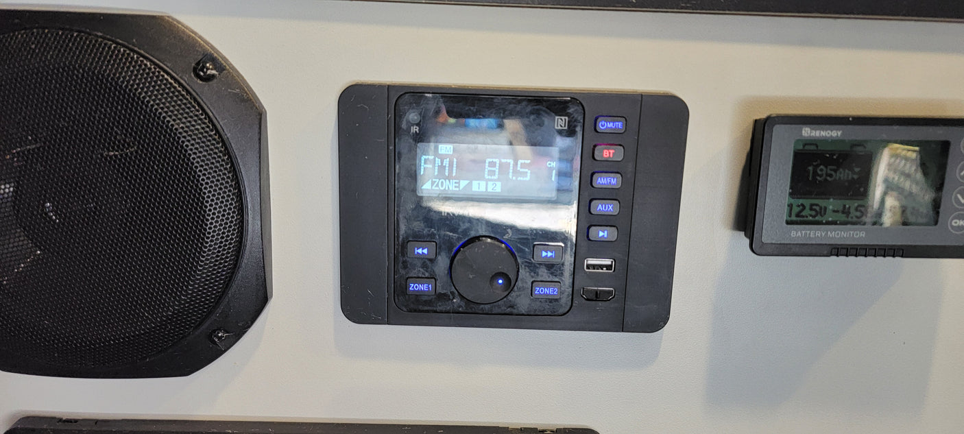 RV rental interior featuring an audio system playing FM 87.5, a speaker, and a Renogy battery monitor at 12.5V.