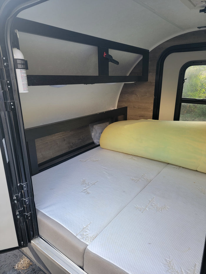 RV rental interior: Comfortable bed with yellow foam topper, overhead storage, and fire extinguisher for safety.