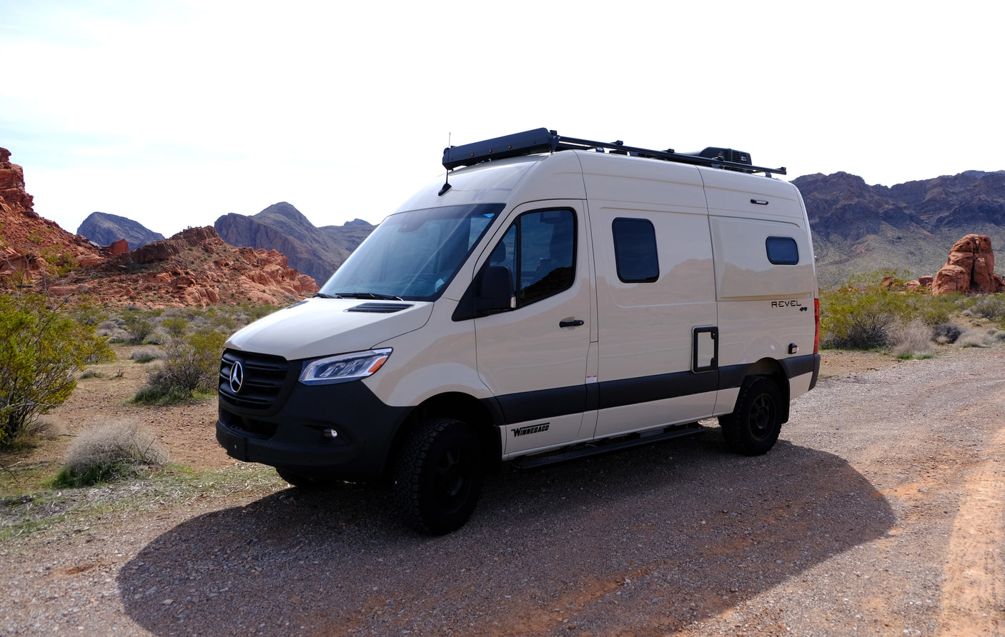 Beige Winnebago Revel 4x4 RV rental on a desert road with red mountains in the background.