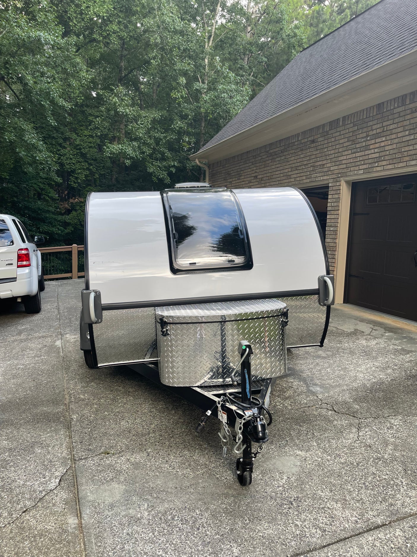 Compact white travel trailer, ideal for an rv rental adventure, parked in a driveway. Features a large front window & storage box.