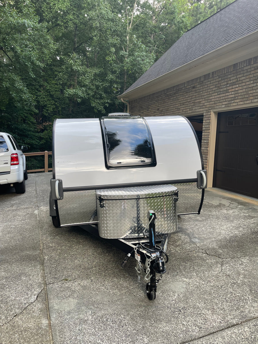 Compact white travel trailer, ideal for an rv rental adventure, parked in a driveway. Features a large front window & storage box.