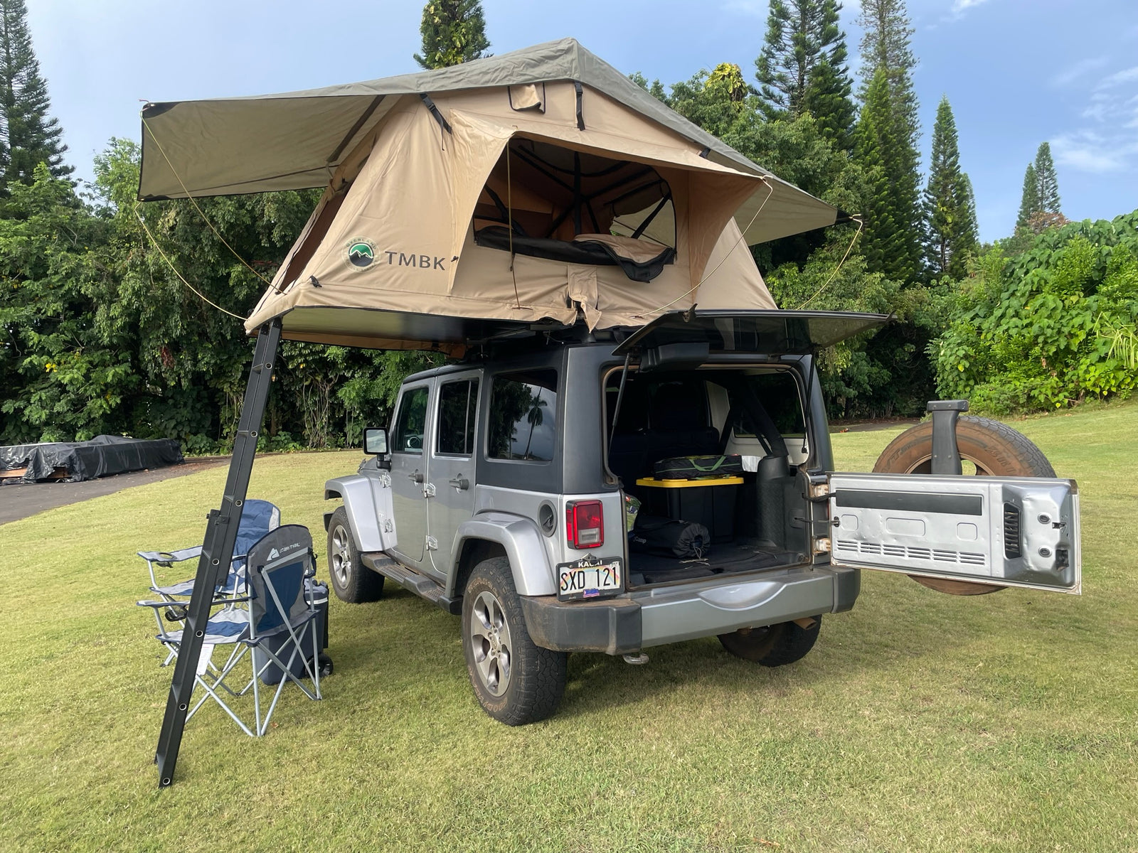 This Jeep RV rental, featuring a deployed rooftop tent, ladder, and camping chairs, is ideal for overland adventures.