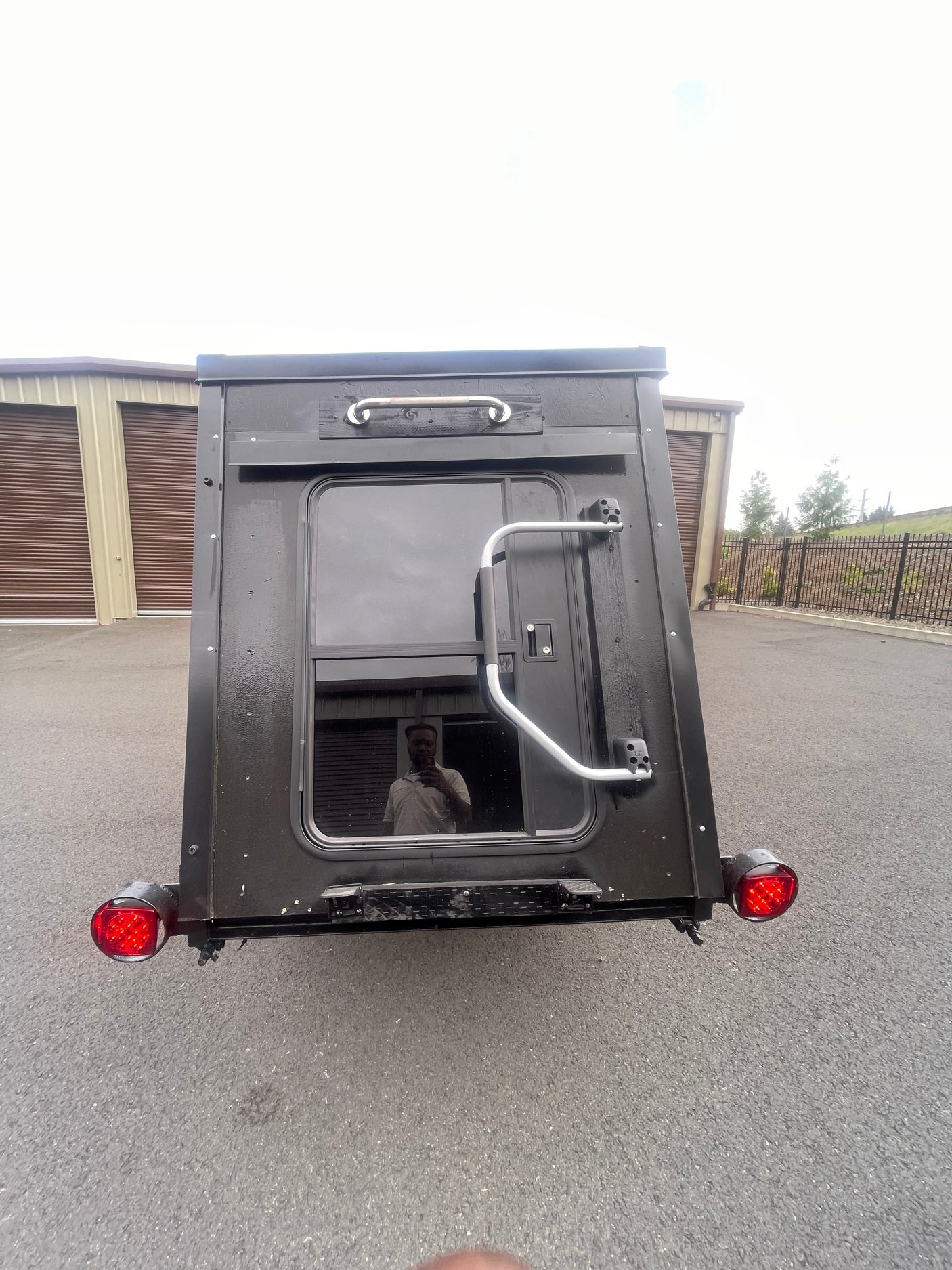 Rear view: compact black RV rental trailer, door, window, grab handles, and red taillights. Ready for adventure.